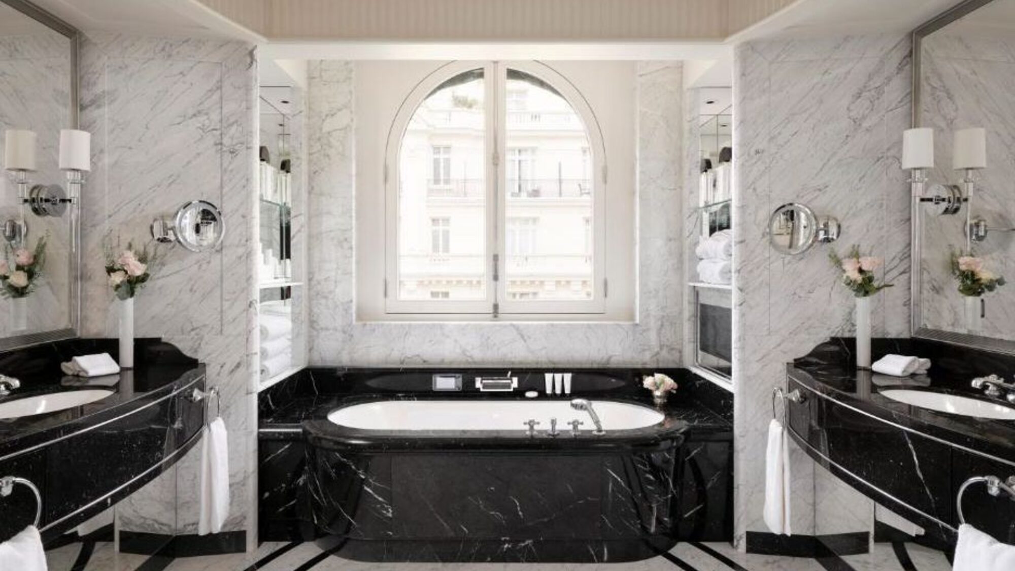 Marble bathroom with a black stone bath surround beneath an arched window